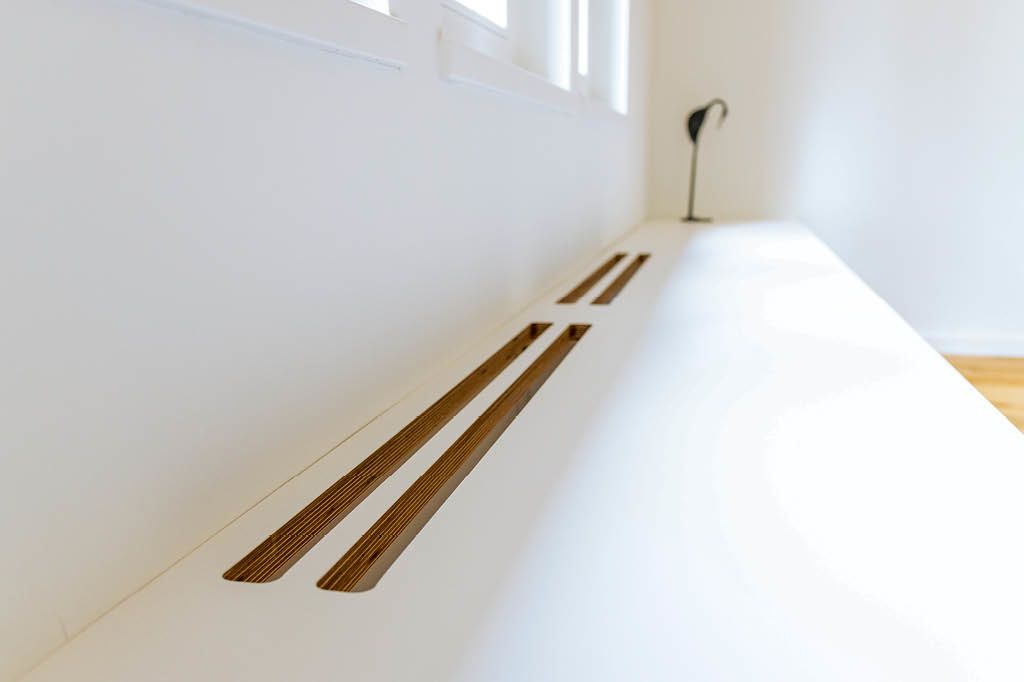 weiße Sitzbank nach Maß vom Tischler aus HPL High Pressure Laminate Multiplex Multiplexplatten mit Lüftungsschlitzen über Heizung Heizkörper